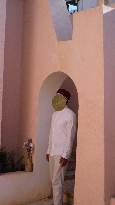 person wearing a red chechia hat and white undercap standing in an archway